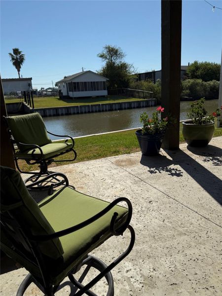 This photo showcases a tranquil patio area with comfortable seating and potted plants, overlooking a serene canal and lawn. Ideal for relaxation and enjoying waterfront views.