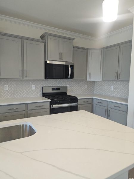 Kitchen with gray cabinets, crown molding, range with gas stovetop, backsplash, and stainless steel microwave