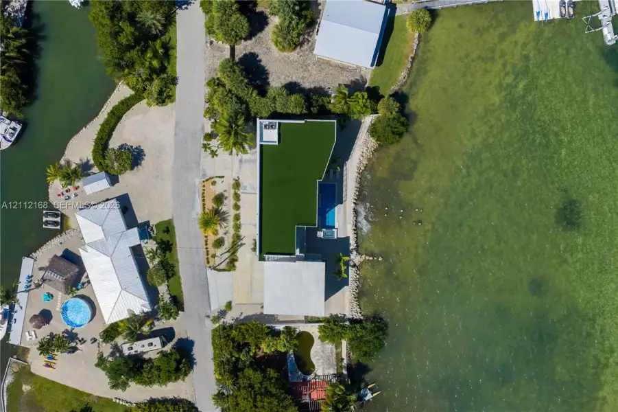 Waterfront estate featuring a direct shoreline, private swimming pool, concrete paved driveway, and artificial turf roof installation Waterfront estate featuring a direct shoreline, private swimming pool, concrete paved driveway, and artificial turf roof installation