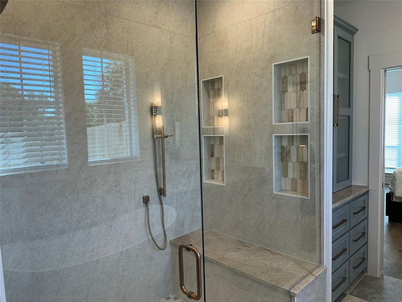 Glass-enclosed shower featuring large format tile, a built-in bench, two integrated display niches with decorative tile, and a handheld shower fixture