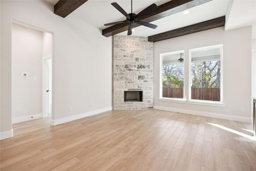 Unfurnished living room featuring beam ceiling, a stone fireplace, ceiling fan, and light hardwood / wood-style floors