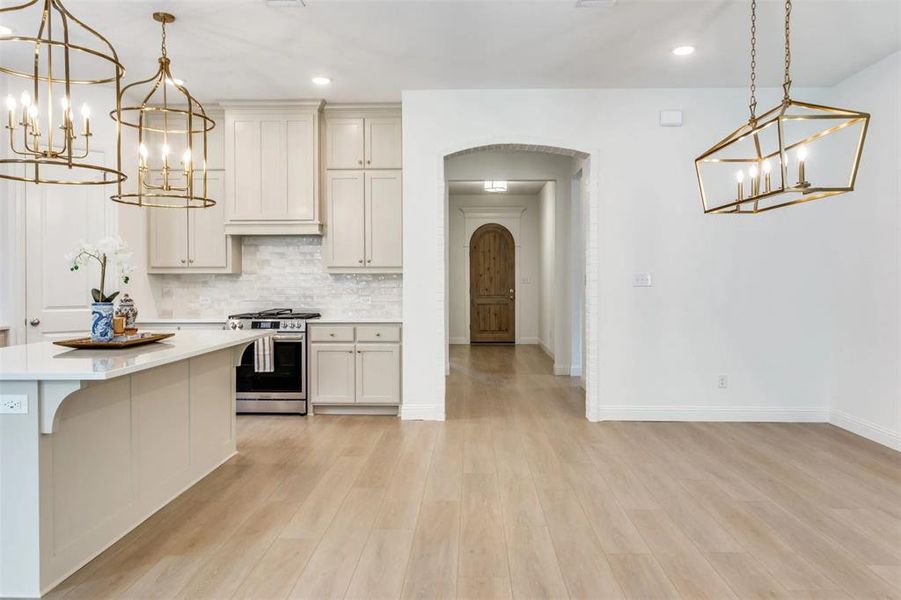 Kitchen featuring a chandelier, hanging light fixtures, arched walkways, stainless steel gas range, and backsplash Kitchen featuring a chandelier, hanging light fixtures, arched walkways, stainless steel gas range, and backsplash