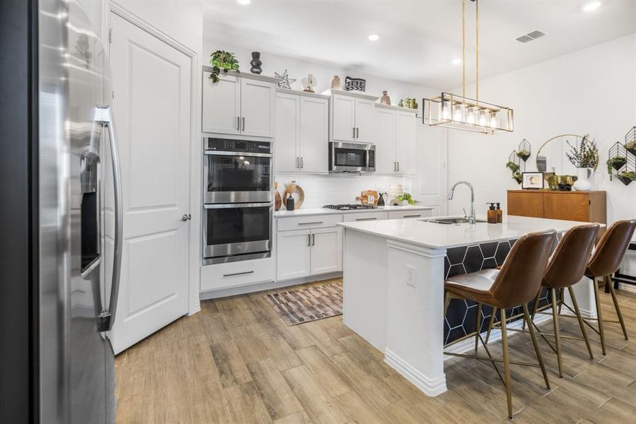 Kitchen featuring stainless steel appliances, tasteful backsplash, a kitchen bar, a center island with sink, and decorative light fixtures Kitchen featuring stainless steel appliances, tasteful backsplash, a kitchen bar, a center island with sink, and decorative light fixtures