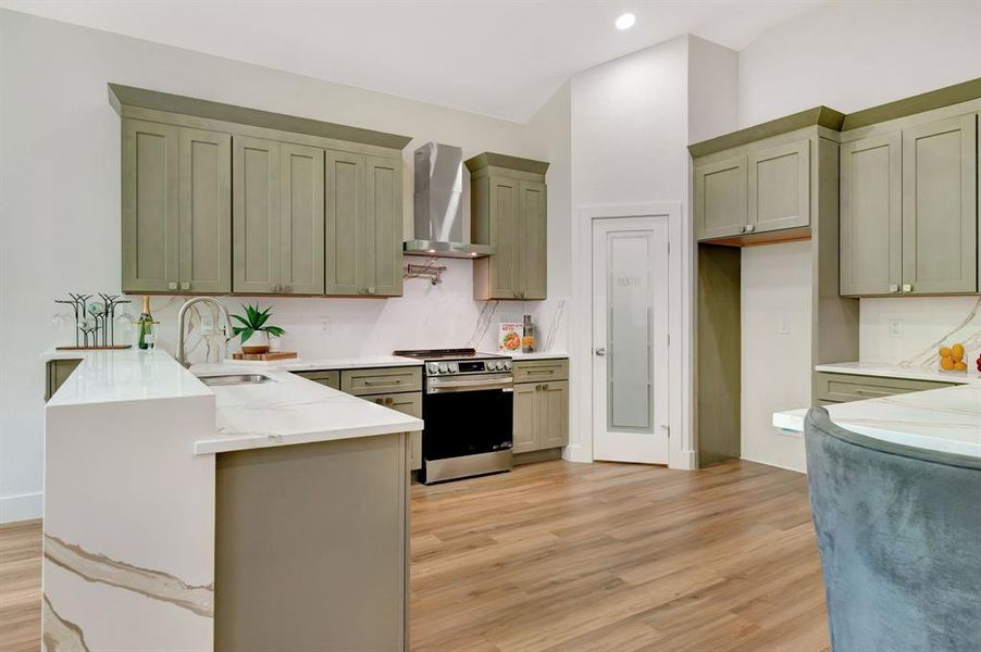 Contemporary kitchen featuring wood-finish flooring, a kitchen island with a waterfall-edge countertop, sage green cabinetry, white subway tile backsplash, and stainless steel appliances Contemporary kitchen featuring wood-finish flooring, a kitchen island with a waterfall-edge countertop, sage green cabinetry, white subway tile backsplash, and stainless steel appliances