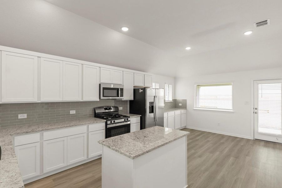 Kitchen with white cabinets, appliances with stainless steel finishes, tasteful backsplash, a center island, and light wood-style floors