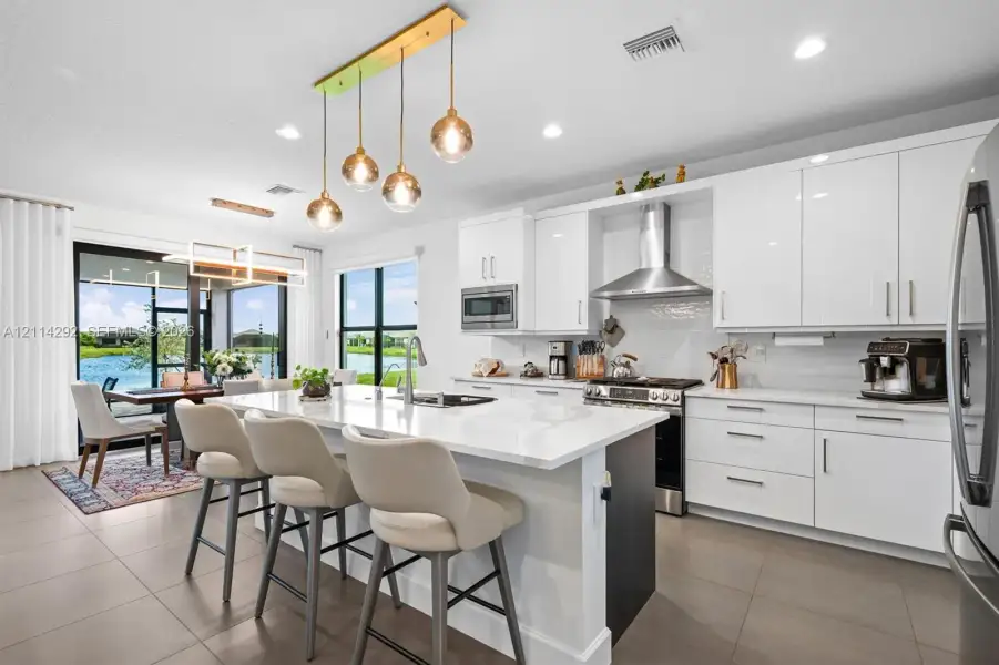 Kitchen featuring high-gloss white cabinetry, a large central island with white quartz countertops, stainless steel appliances, and multi-pendant lighting