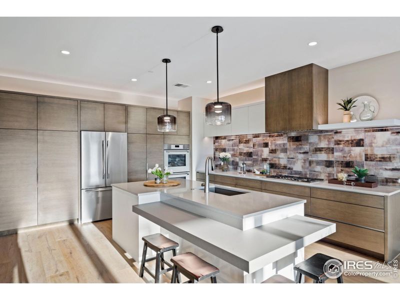 Welcome to unit #401! There is a ton of cabinet space from custom cabinet maker, Genesis Innovations, in this gorgeous kitchen with bespoke, glass backsplash, a two tiered island, double oven and gas range (plumbed for induction).