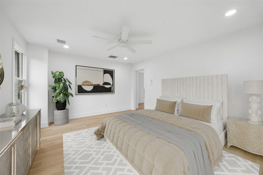The primary suite offers a spacious layout with room for additional seating, oversized furnishings, or a private lounge setup while maintaining a clean and comfortable flow throughout the space. Engineered wood flooring, recessed lighting, and large-scale windows continue the home’s modern architectural aesthetic. (digitally staged)