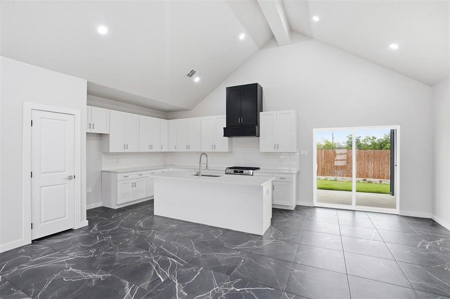 Contemporary kitchen featuring an island with integrated sink, white cabinetry, and contrasting black range hood