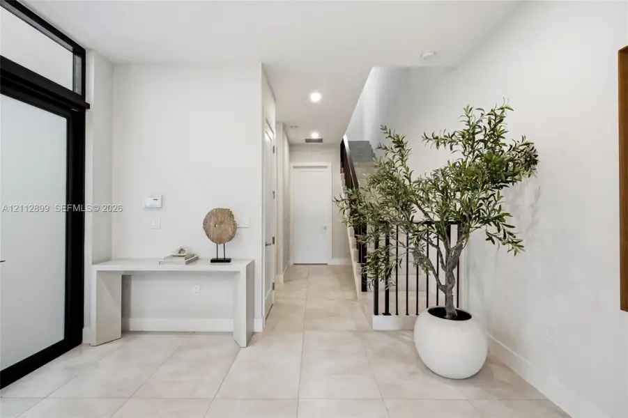 Entryway featuring large-format tile flooring, a glass-paneled front door with black trim, recessed lighting, and a staircase with black metal balusters