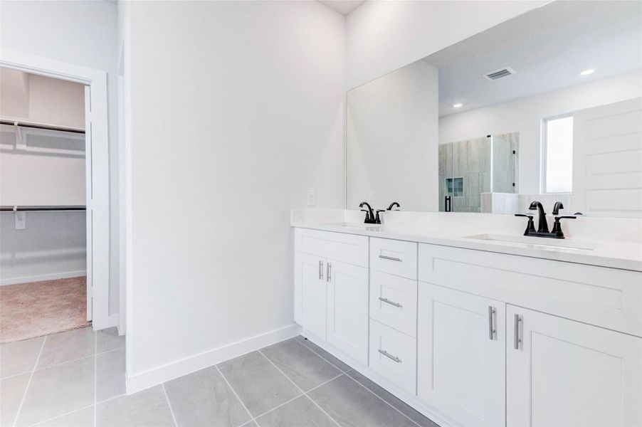 The spa-like primary bath features a sleek double-sink vanity with quartz countertops and ample storage. A full-width mirror expands the space visually, while matte black fixtures add a touch of modern elegance to your morning and evening routines.