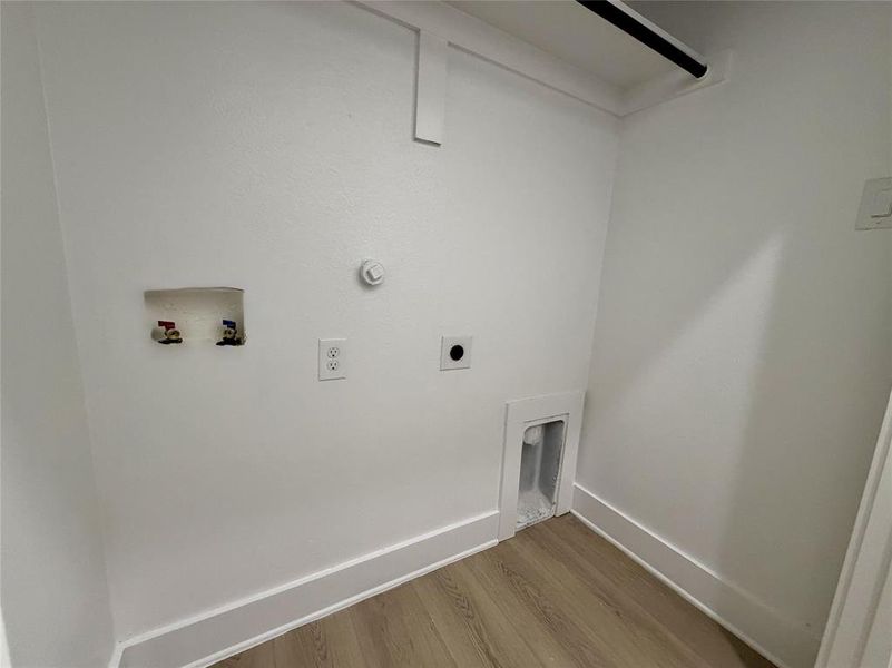 Dedicated laundry alcove featuring light wood-finish flooring, white walls, and a hanging rod Dedicated laundry alcove featuring light wood-finish flooring, white walls, and a hanging rod