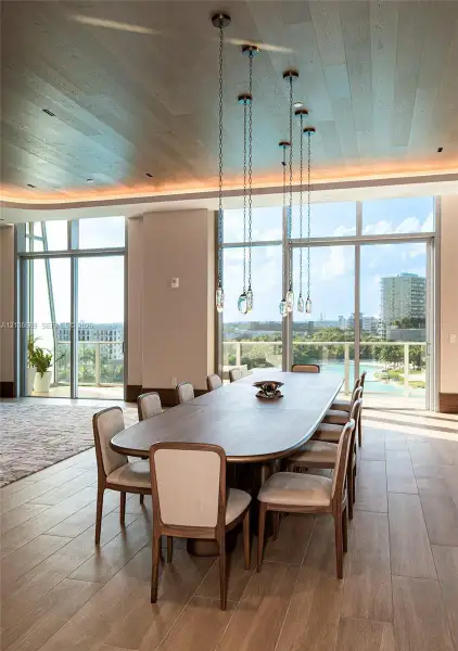 Floor-to-ceiling windows, wood-finish plank flooring, wood-paneled ceiling with recessed cove lighting, and a multi-pendant chain chandelier
