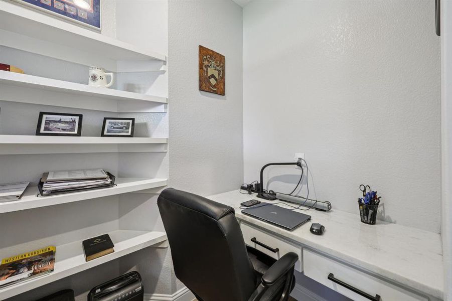 Home office featuring a textured wall, built in study area, and built in shelves Home office featuring a textured wall, built in study area, and built in shelves