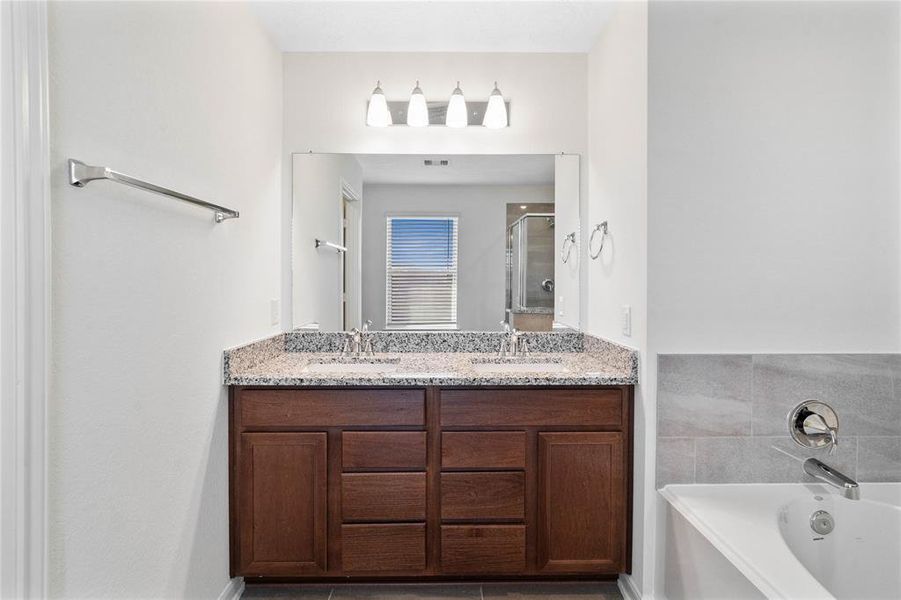 This primary bathroom is definitely move-in ready! Featuring an oversized framed walk-in shower with tile surround, separate garden tub for soaking after a long day with custom tile detailing, stained cabinets with light countertops, high ceilings, neutral paint, sleek and modern finishes.