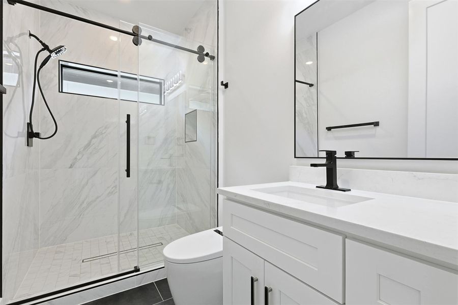 Another bathroom includes a walk-in shower with floor-to-ceiling marble-patterned tile and a sliding glass door.