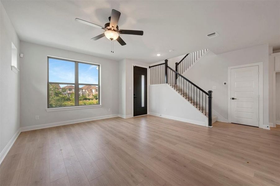 Spacious living area featuring wood-finish flooring, a contemporary ceiling fan, and a prominent staircase with black metal balusters