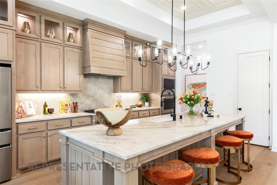 Kitchen featuring a breakfast bar, a tray ceiling, custom exhaust hood, and light wood-type flooring Kitchen featuring a breakfast bar, a tray ceiling, custom exhaust hood, and light wood-type flooring