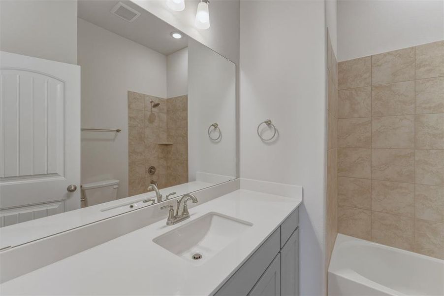 Bathroom vanity featuring a single basin sink, brushed nickel faucet, large mirror, and light gray cabinetry