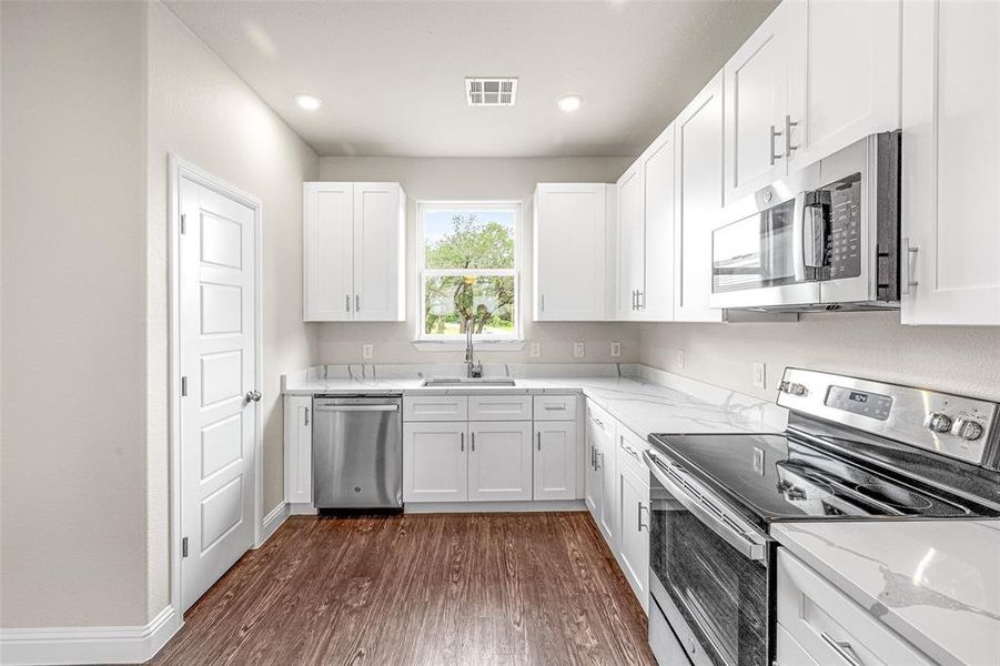 Kitchen featuring light stone counters, dark hardwood / wood-style floors, white cabinets, sink, and appliances with stainless steel finishes