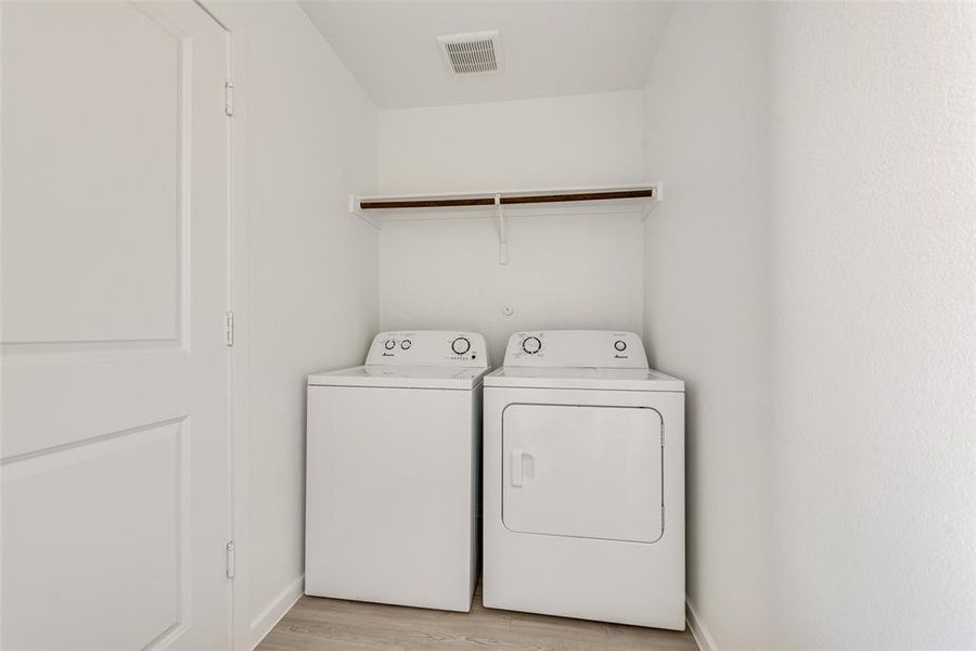 Clothes washing area with light wood-type flooring and separate washer and dryer