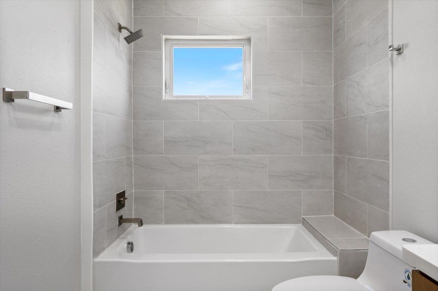 A windowed shower/tub combination with gray tiled walls offers a serene bathing experience.