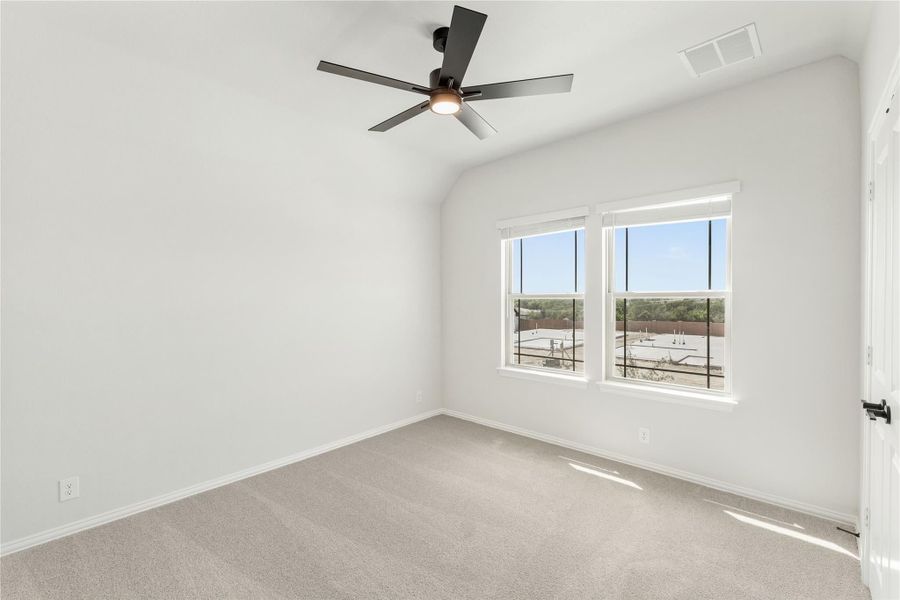 Empty bedroom with vaulted ceiling, black ceiling fan, carpet flooring, and double windows with outdoor views.