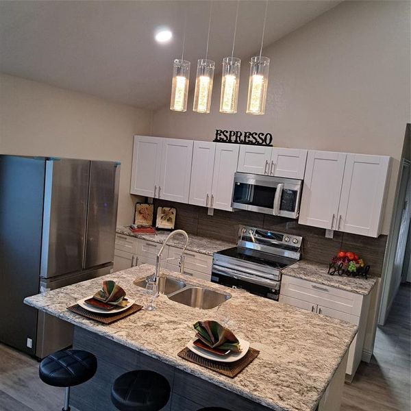 Kitchen with sink, stainless steel appliances, pendant lighting, white cabinets, and a center island with sink