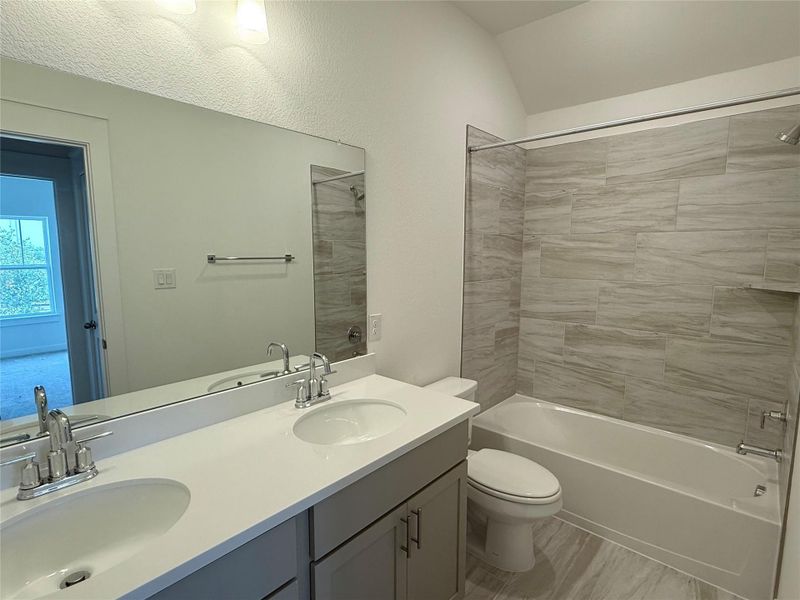 Full bath featuring double vanity, tub / shower combination, and vaulted ceiling