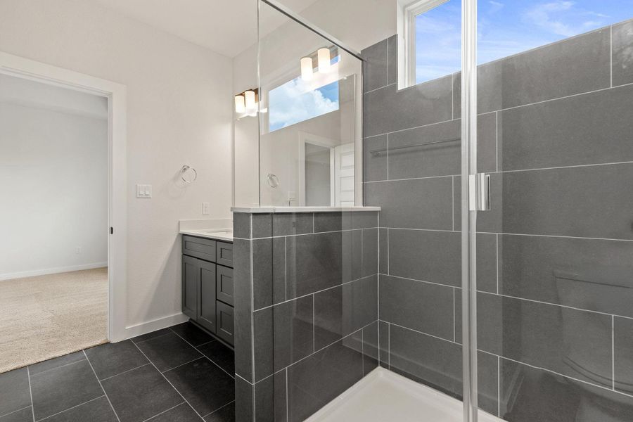 A well-lit bathroom with contemporary grey tiling and a spacious shower.