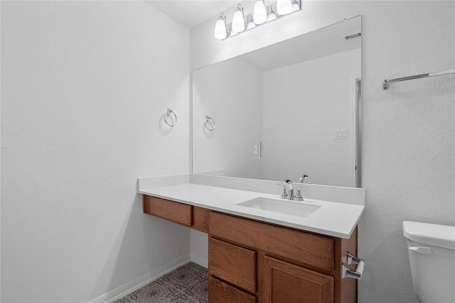 Secondary bath features tile flooring, stained wood cabinet, beautiful light countertops, mirror, dark, sleek fixtures and modern finishes.