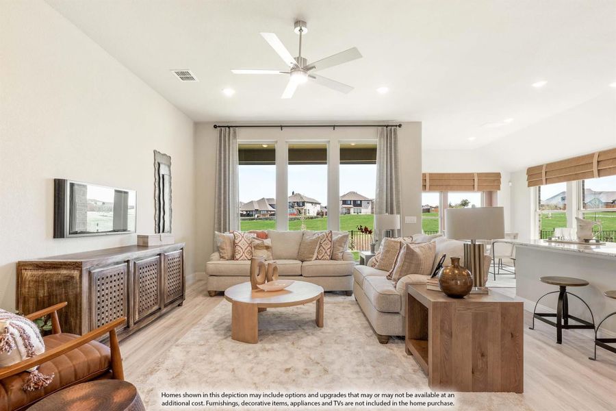 Open living room with beige sofas, ceiling fan, large windows, and light hardwood floors