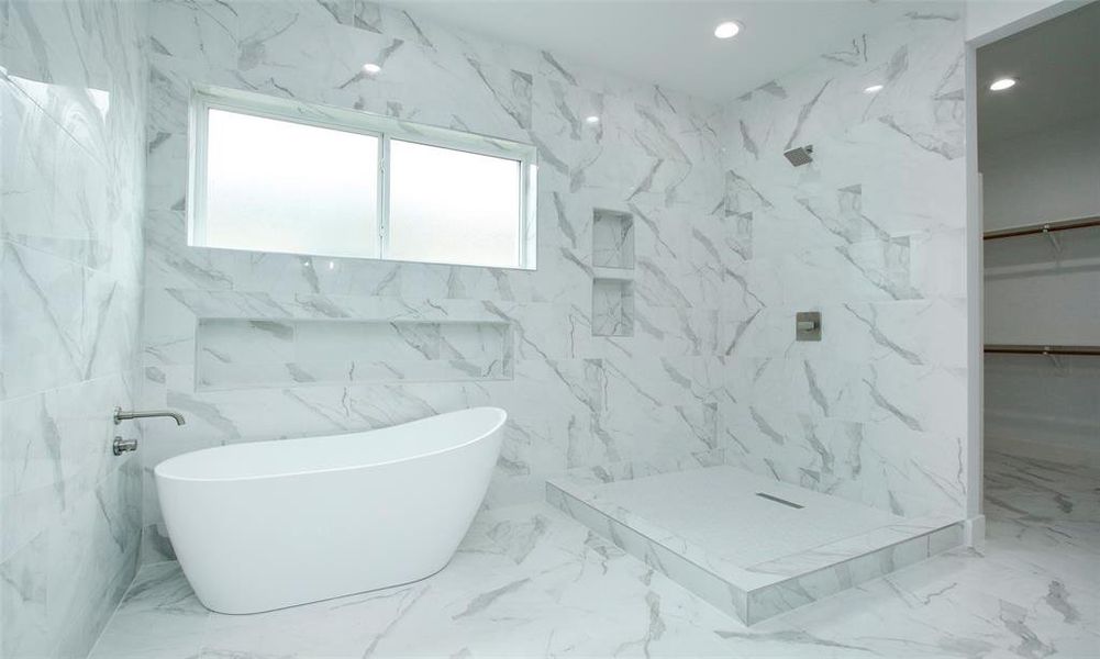 Modern bathroom featuring sleek white freestanding tub, walk-in shower with glass door, and marble-look tiles throughout. It includes a frosted glass window for natural light and privacy.