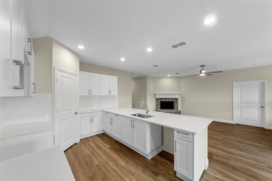 Open-concept kitchen featuring white cabinetry with brushed nickel hardware, white countertops, subway tile backsplash, and wood-finish flooring