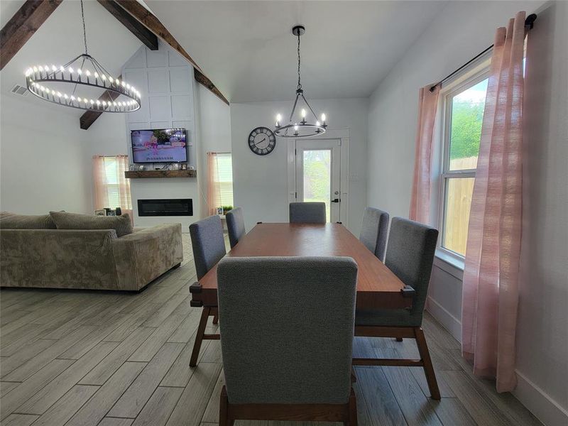 Dining space with a chandelier, wood finished floors, vaulted ceiling, and a fireplace
