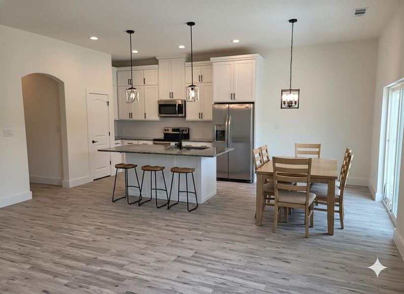 The open-concept kitchen and dining area features white cabinetry, stainless steel appliances, a kitchen island with seating, and light-colored flooring