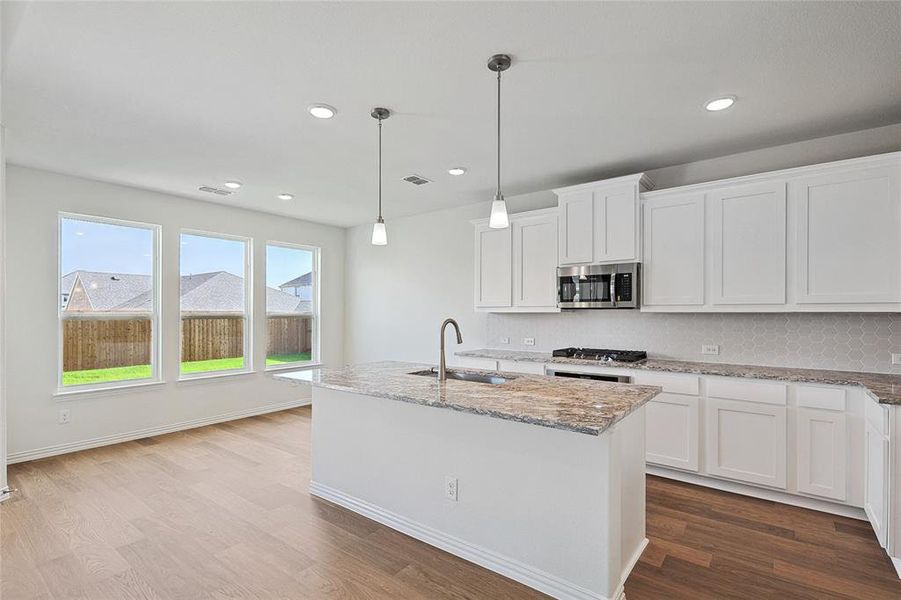 Kitchen featuring white cabinetry, decorative backsplash, an island with sink, light wood-type flooring, and sink