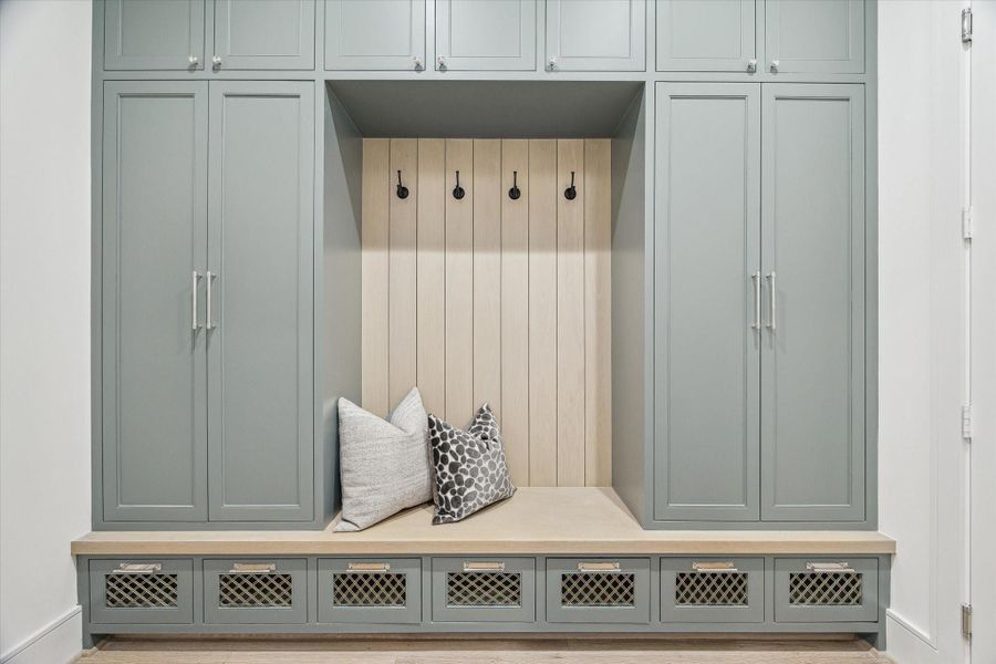 The mud room houses floor-to-ceiling cabinetry and a white oak bench. Plenty of space to store outwear, sportsgear, and more with ease. The dark tones complement the oak nicely.