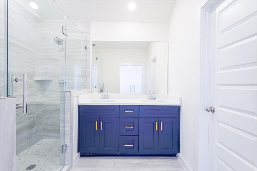This bathroom features a modern design with a glass-enclosed shower, marble-style tiles, a sleek double vanity with dark cabinetry, and stylish fixtures.