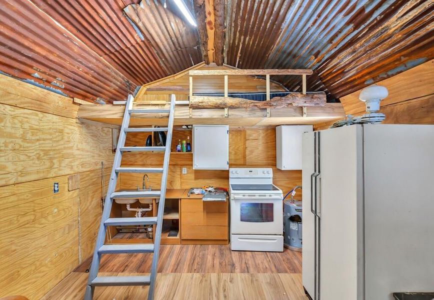 Kitchen featuring light wood-type flooring, white appliances, wooden walls, and vaulted ceiling