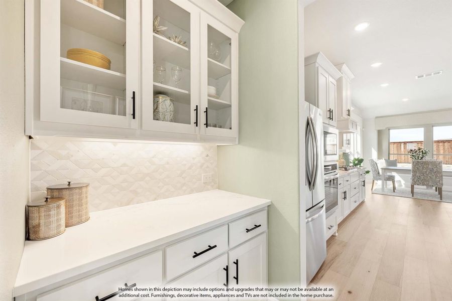 Kitchen with white cabinets, glass-front uppers, geometric tile backsplash, and stainless steel refrigerator