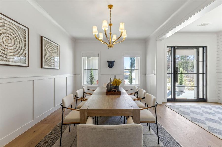 Dining space with visible vents, a decorative wall, ornamental molding, wood finished floors, and a chandelier Dining space with visible vents, a decorative wall, ornamental molding, wood finished floors, and a chandelier