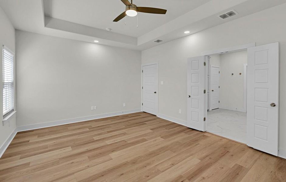 Unfurnished bedroom featuring a raised ceiling, a ceiling fan, light wood-style floors, and recessed lighting