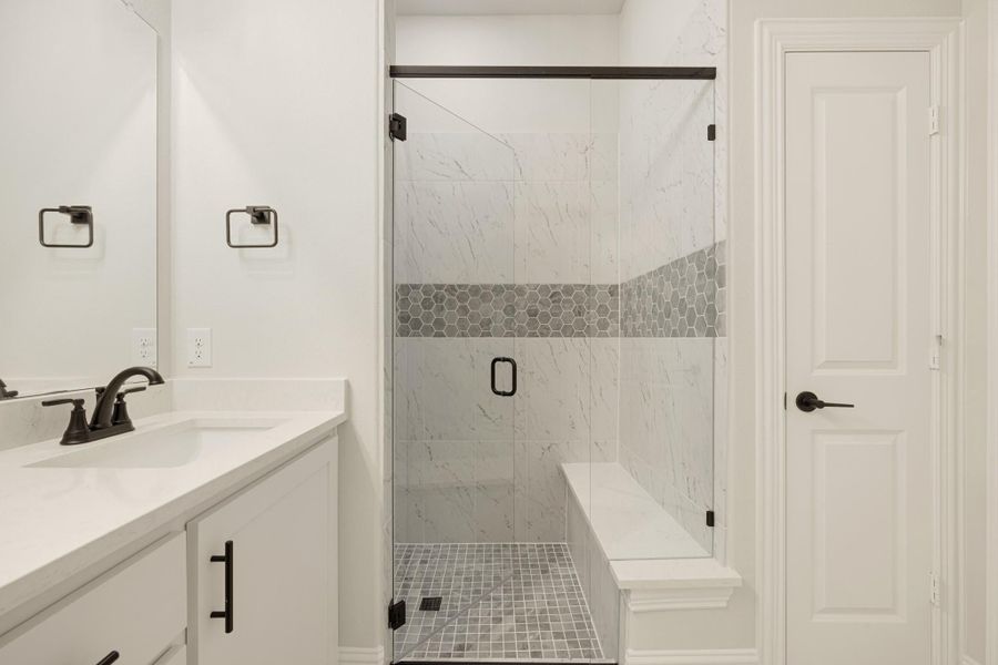Bathroom with glass walk-in shower, marble tile walls, built-in bench, and white vanity with dark hardware