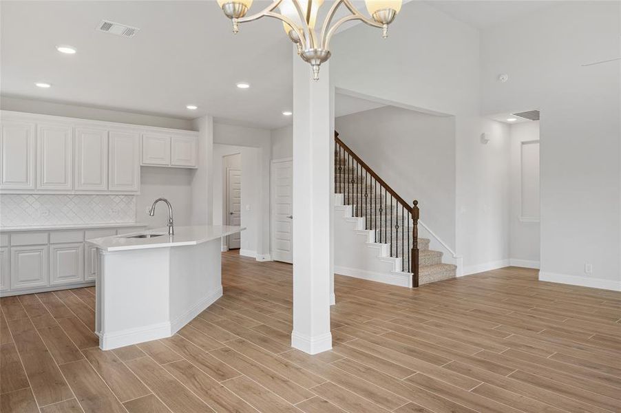 Kitchen with white cabinets, tasteful backsplash, light wood-type flooring, a center island with sink, and recessed lighting