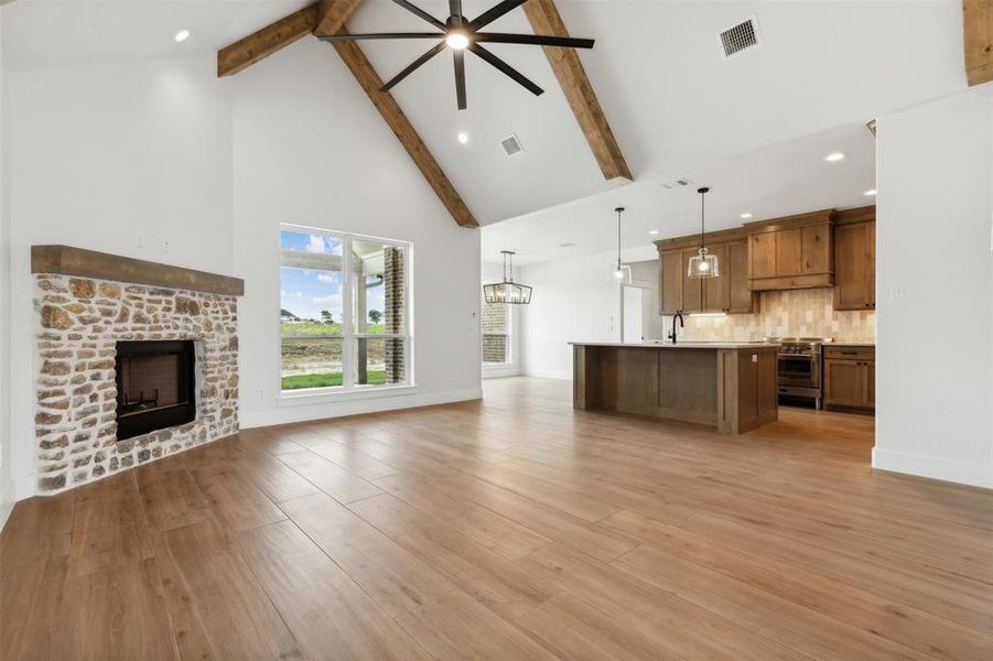 Unfurnished living room with high vaulted ceiling, ceiling fan with notable chandelier, light wood-type flooring, and beam ceiling