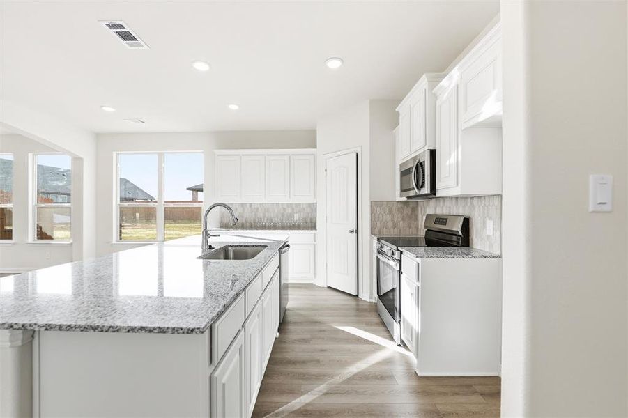 Kitchen with white cabinets, stainless steel appliances, light stone counters, an island with sink, and recessed lighting