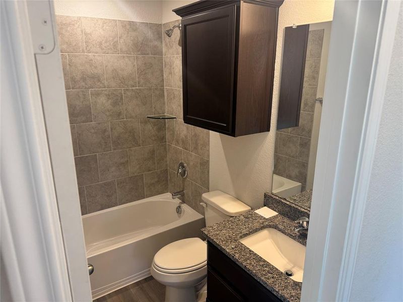 Bathroom with a textured wall, shower combination, vanity, and dark wood-style floors Bathroom with a textured wall, shower combination, vanity, and dark wood-style floors