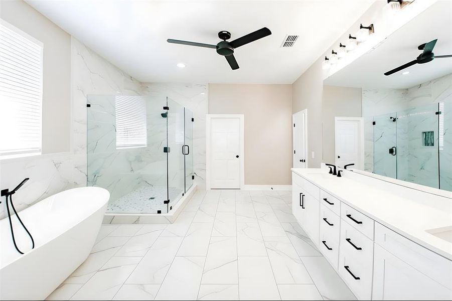 Full bath featuring a soaking tub, double vanity, ceiling fan, a marble finish shower, and light marble finish floors Full bath featuring a soaking tub, double vanity, ceiling fan, a marble finish shower, and light marble finish floors