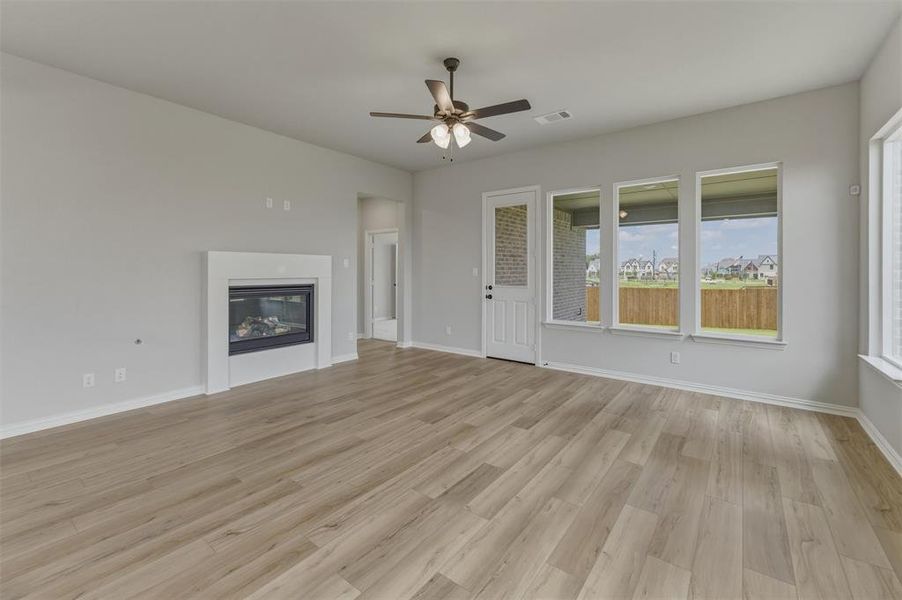 Spacious interior featuring wood-finish flooring, a contemporary fireplace with a white mantel, multiple large windows, and a ceiling fan with integrated lighting Spacious interior featuring wood-finish flooring, a contemporary fireplace with a white mantel, multiple large windows, and a ceiling fan with integrated lighting